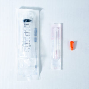 A packaged syringe, a packaged needle, and an orange needle cap on a white surface.
