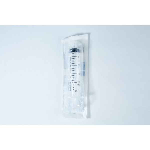 A packaged disposable syringe lies on a white surface, sealed in transparent plastic wrapping.