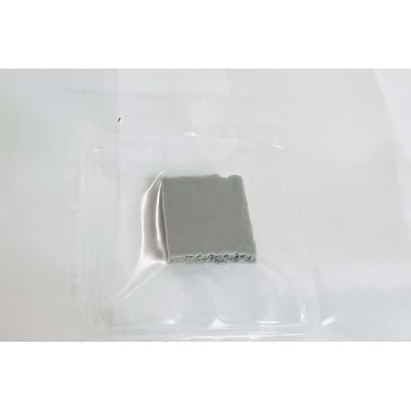 A small, square piece of grey material on a clear plastic tray against a white background.