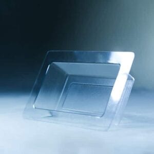 A Mycelium Mould Growth form -Brick (Reusable) stands upright on a smooth, misty surface, its organic curves reflected in the transparent plastic food container lid beside it.