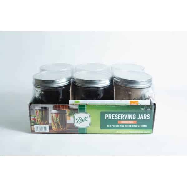 A set of six Ball Mason pint jars with wide mouths are organised in a cardboard box labelled "Preserving Jars" and shown against a white background.