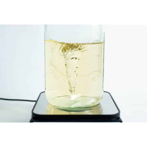 A vortex swirls in a yellow liquid within a glass jar on the Magnetic Stirrer Ciblanc 3500rpm, highlighting the stirring precision of this device.