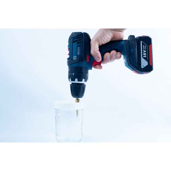 A hand holds a Drill Bit for hole sizes 3mm-12mm Titanium Coated attached to a power drill, positioned above a glass jar on a white background.