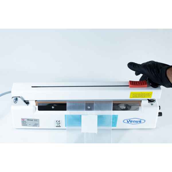 A gloved hand operates a Heat Sealer 30cm Seal Width 5mm with cutter and magnet, sealing a plastic bag securely inside the machine.