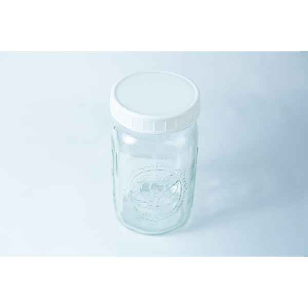 Photographed on a light blue background, this clear glass jar features a plain white plastic lid, designed to fit wide mouth mason jars with 86mm Mason Jar Lids | Wide Mouth | Plain White Plastic Lids.