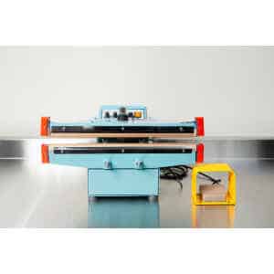 A Heat Sealer 450mm with 10mm Seal | Benchtop Model, featuring control knobs and a yellow foot pedal, sits on a metal counter, designed for reliable industrial sealing.