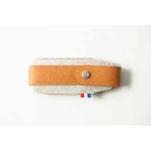 The Opinel Sheath - Brown, made from tan leather and grey felt with a button fastening, rests on a white surface.