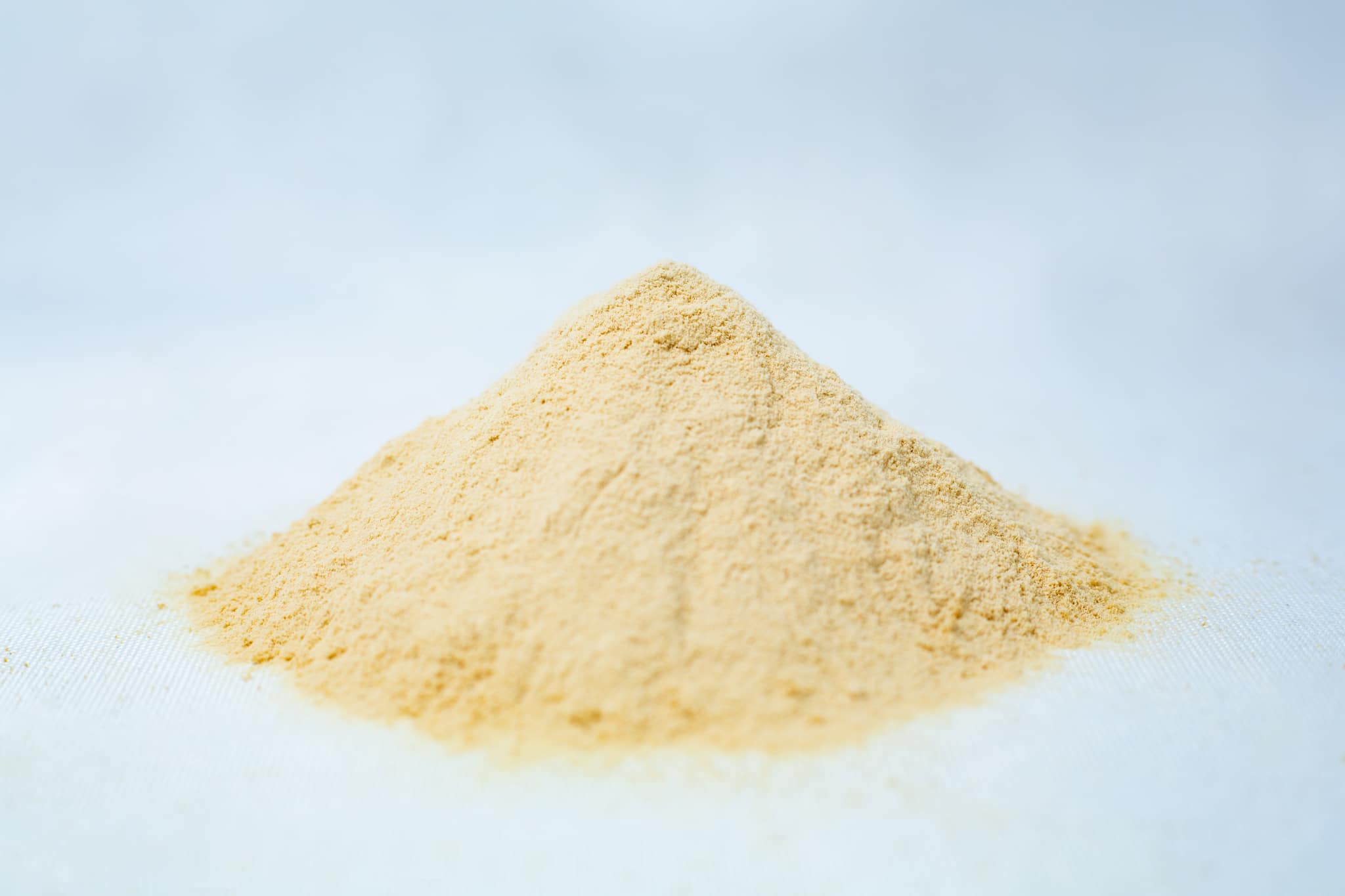A small mound of fine, light yellow Mycological Soya Peptone powder for agar media use in microbiology labs rests on a white surface against a soft, blurred background.