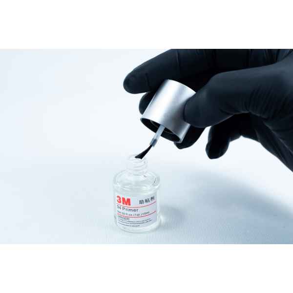 A gloved hand holds a brush applicator over an open bottle of Primer 94 multisurface for 3M glue 10ml on a white background.
