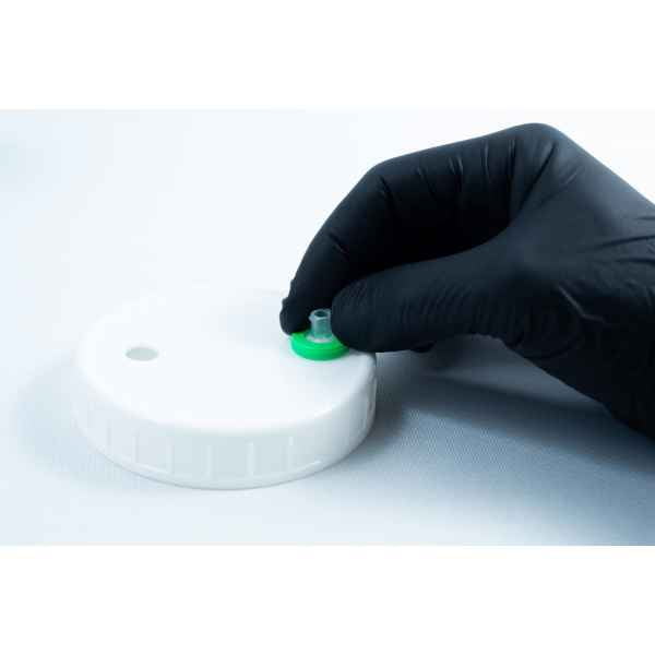 A gloved hand holds a green-capped valve on a white plastic lid, commonly used for storing Primer 94 multisurface for 3M glue 10ml, against a white background.