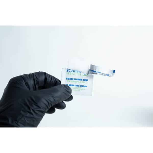A hand in a black glove holds an open packet of Sterile Alcohol Wipes / Swabs / Pads (Box of 100) against a white background.