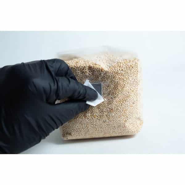 A gloved hand cleans a plastic bag of white grains on a white surface using Sterile Alcohol Wipes / Swabs / Pads (Box of 100).