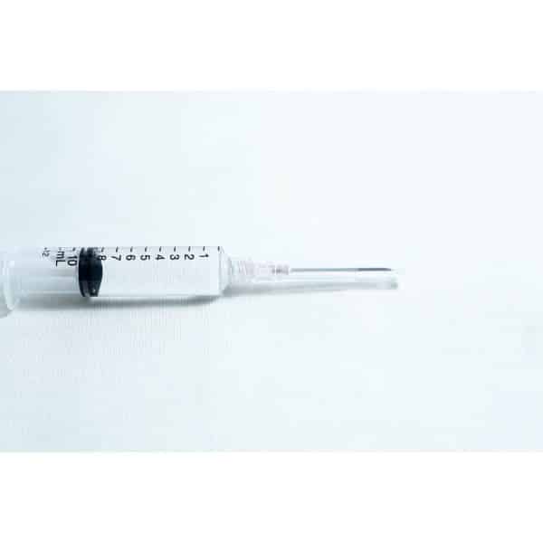A syringe with clear liquid rests on a white surface, fitted with a sterile 18G hypodermic needle from a box of 100pcs.