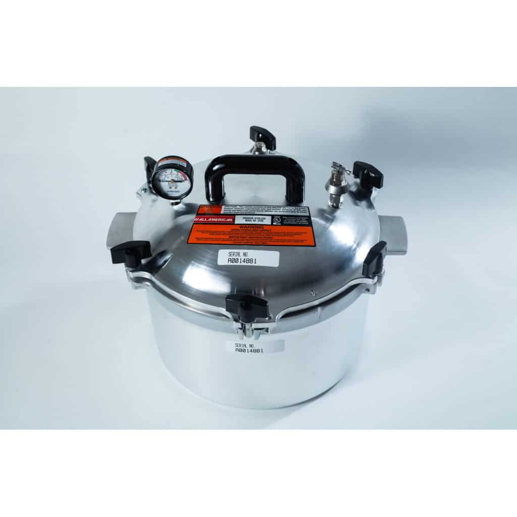 A stainless steel pressure cooker with a pressure gauge, black handles, and warning labels on the lid.