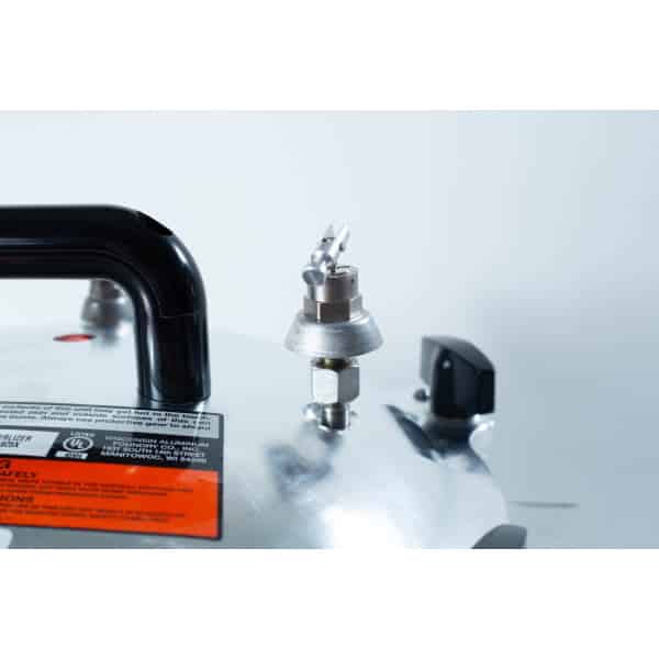 Close-up of an All American Wingnut pressure cooker lid featuring the pressure valve, handle, and safety instructions label.