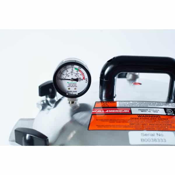 Close-up of a pressure gauge and warning labels on a stainless steel pressure steriliser.