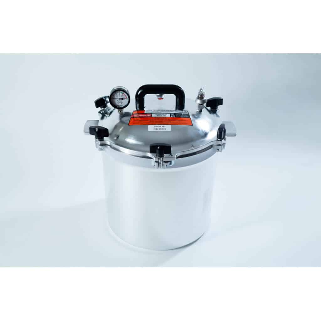 A stainless steel pressure cooker with a gauge, handle, and safety valves on a white background.