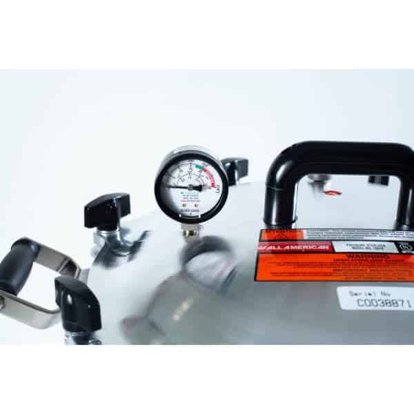Close-up of the All American Wingnut pressure canner lid featuring a pressure gauge, handles, and warning labels.