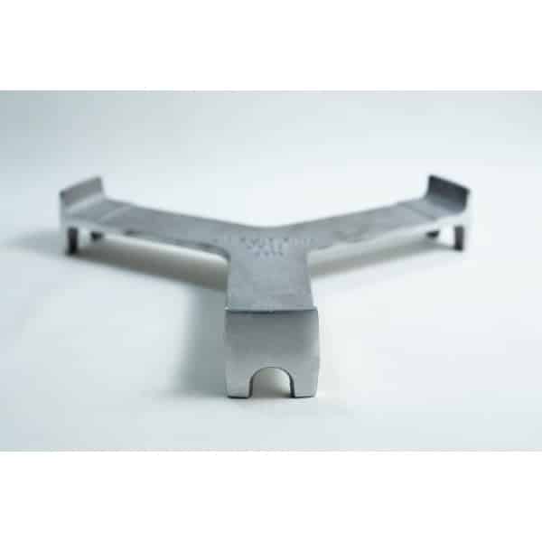 A metal trivet with three arms rests on a white surface, viewed from a low front angle.