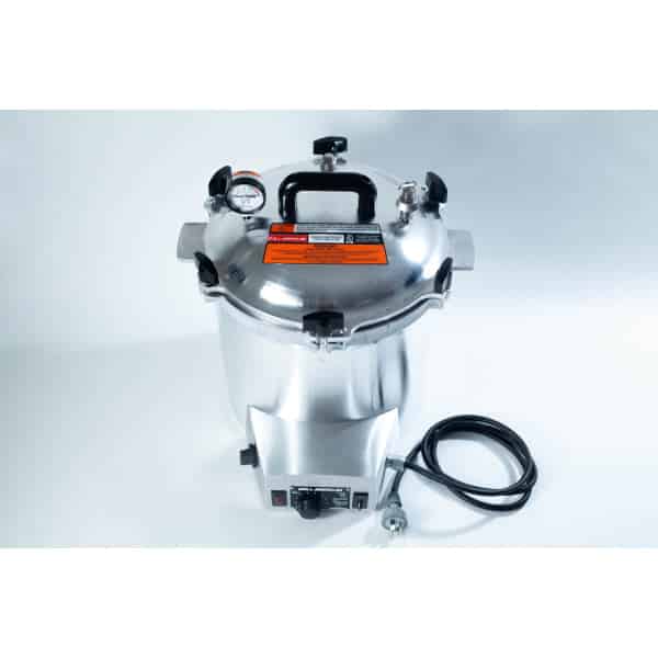 A stainless steel pressure cooker with a gauge, black handles, and an attached power lead on a white background.