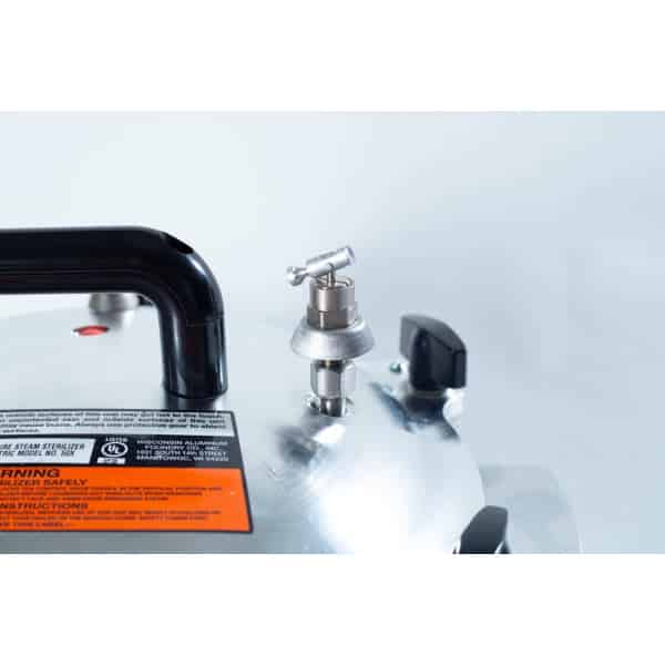 Close-up of a pressure cooker lid showing the pressure release valve, handle, and warning label.