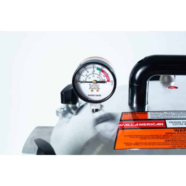 Close-up of a pressure gauge on a metal appliance with caution and warning labels visible.