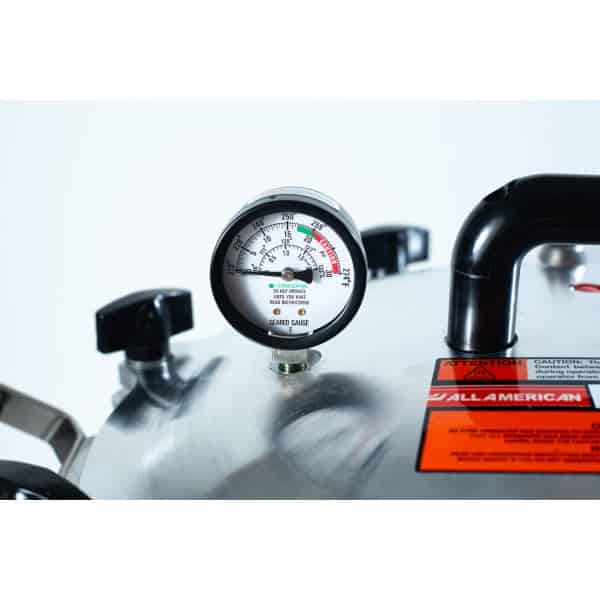 Close-up of a pressure gauge on a metal pressure cooker with caution labels visible.