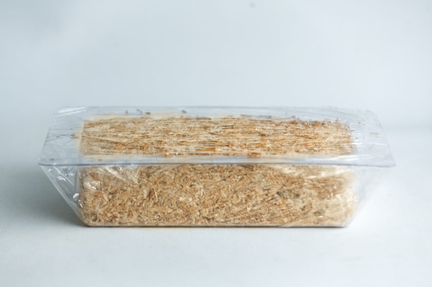 Mycelium Mold Growth form -Brick (Reusable) 12 A block of shredded wheat cereal in a clear plastic tray with a transparent wrapper.