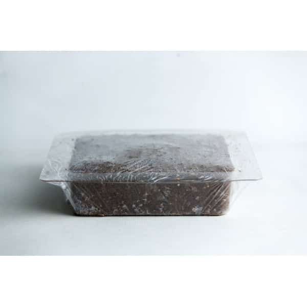 A rectangular block of soil in a plastic container covered with clear plastic film.