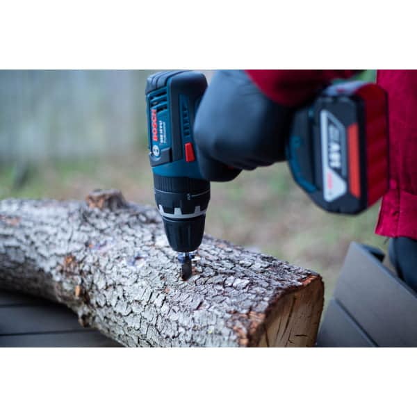 A person drills into a tree log using a cordless power drill outdoors.