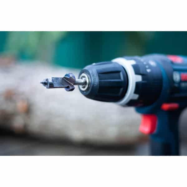 Close-up of a power drill with a drill bit attached, shown in an outdoor setting.