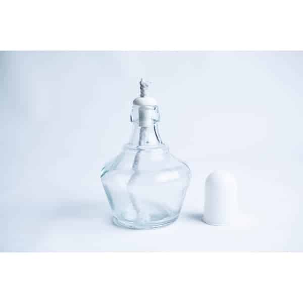 Clear glass perfume bottle with a stopper and white cap placed beside it on a white background.
