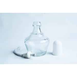 A small empty glass bottle with its white cap and a wick placed beside it on a white background.