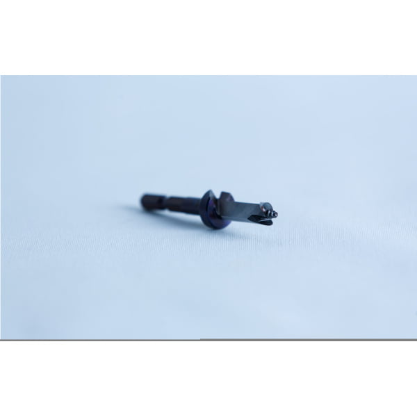 A close-up of a small metal tool or drill bit on a light blue surface with a blurred background.