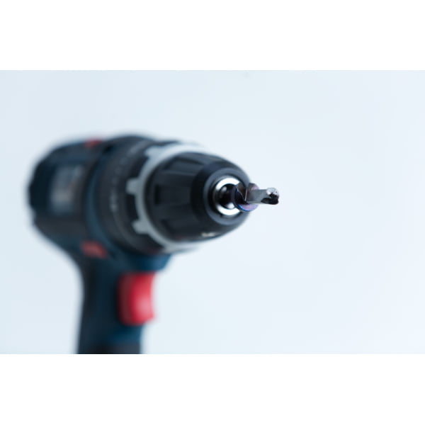 Close-up of a cordless power drill with a screwdriver bit, focussed on the bit against a white background.