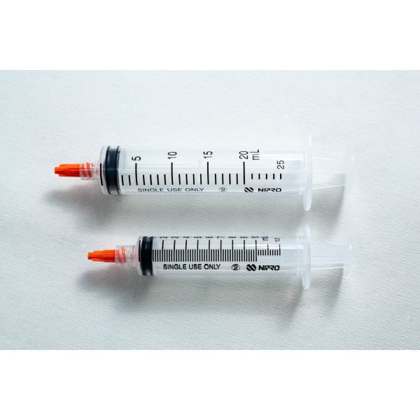 Two plastic syringes with orange caps lying side by side on a white surface.