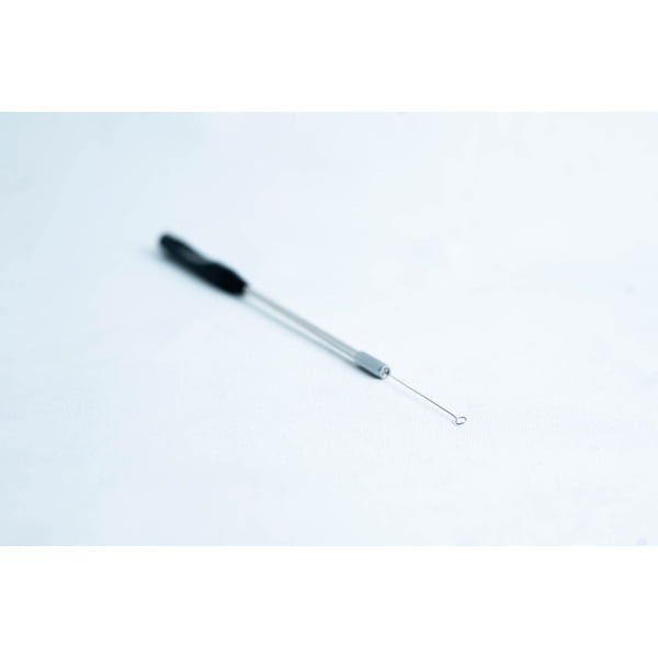 A close-up of a metal blackhead remover tool on a white surface.
