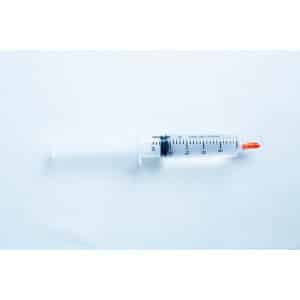 A plastic syringe with a red cap placed on a light blue surface.