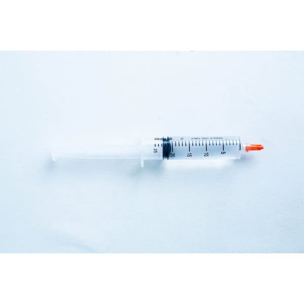 A plastic syringe with a red cap placed on a light blue surface.