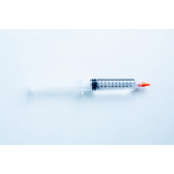 A plastic syringe with a red cap and black measurement markings lies on a white surface.
