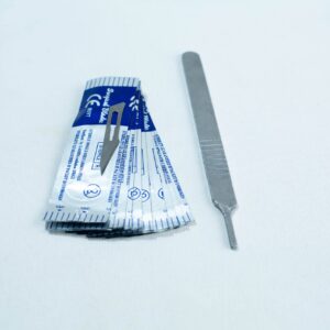 A scalpel handle next to several individually wrapped scalpel blades on a white surface.