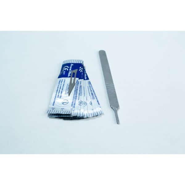 A scalpel handle next to several individually wrapped scalpel blades on a white surface.