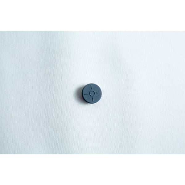 A single dark grey button with four holes on a plain white fabric background.