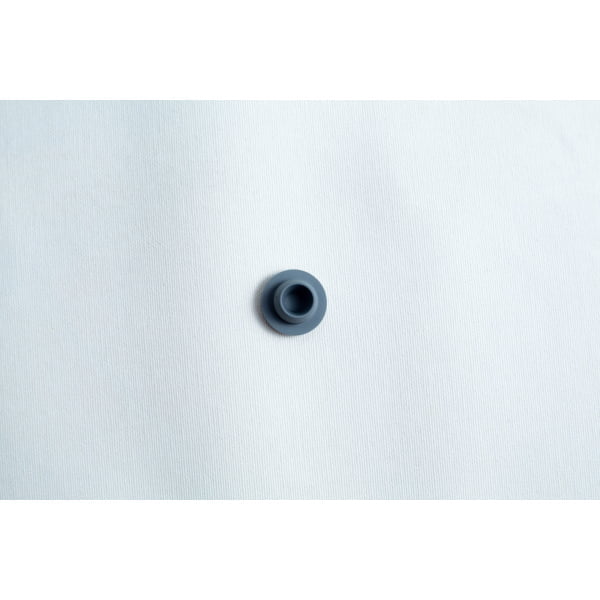 A single dark grey button on a plain white textured fabric background.