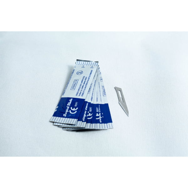 Several wrapped surgical blades and one unwrapped blade on a white surface.