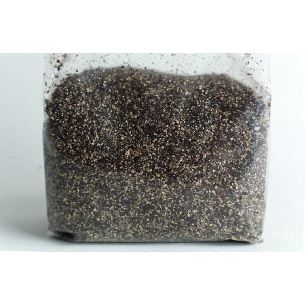 A clear plastic bag filled with coarse, dark soil or sand on a white surface.
