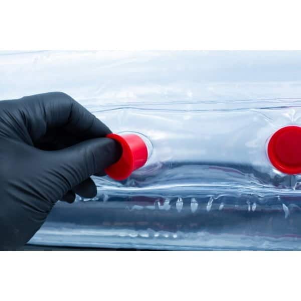 Gloved hand opening a red cap on a clear plastic inflatable or medical isolation chamber.
