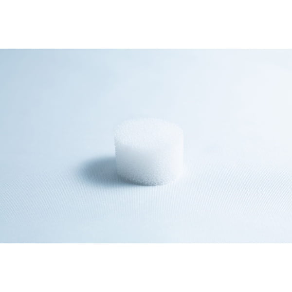 A small, white, cylindrical foam object sits on a light blue surface with soft lighting.