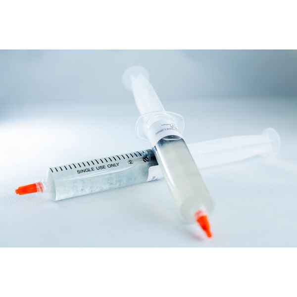 Two single-use syringes with orange caps containing Mushroom Liquid Culture | Wood Ear | Auricularia auricula-judae lie on a white surface, one filled with a clear liquid.