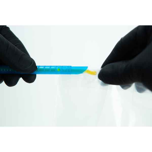 Gloved hands handling a blue plastic tool with yellow substance over a clear plastic bag.
